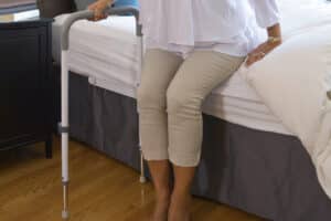 Photo of a woman using a pivoting bed rail (the HealthCraft Smart-Rail) to get herself up out of bed.