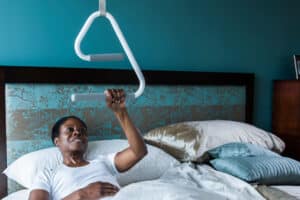 Photo of a woman in bed using an overhead trapeze to lift herself into an upright position.