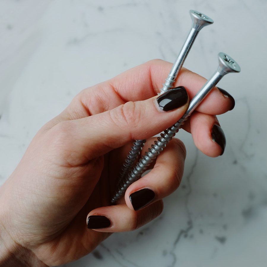 A hand with nails painted black holding screws