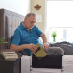 Man sitting up in bed, putting a book into the pouch on his bedrail