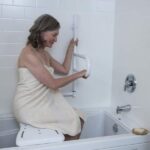 Woman sitting on a bath bench in the bathtub, holding the DependaBar for safety