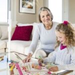 Elderly woman sitting with grand-daughter drawing in living room.