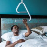 Woman using the e2 Ceiling Mount Trapeze to help sit up in bed