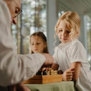 grand-father teaching his two granddaughters how to play chess