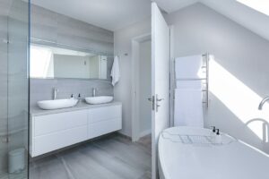 a white themed bathroom with two sinks, glass shower, and elevated tub entrance.