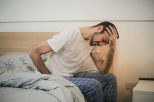 Man stressed out with his hand in his hand, looking down at the floor while sitting on the edge of the bed.