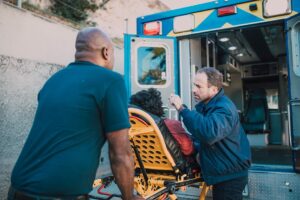 An individual on a gurney being helped into an ambulance by two men.