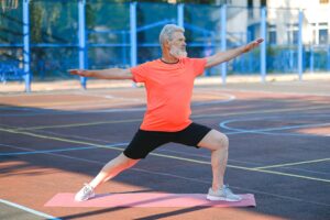 Photo of a man with white hair and a beard exercising on an outdoor basketball court.