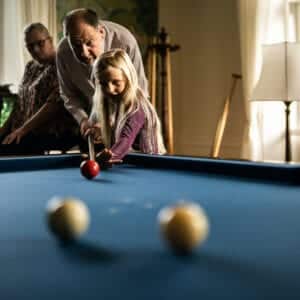 father teaching his daughter how to play pool. She aims to hit the red ball into to other balls