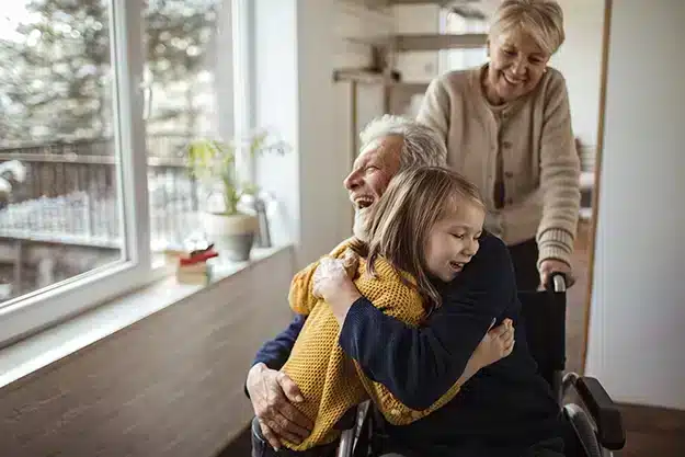 Grandchildren hugging grandpa in wheelchair.